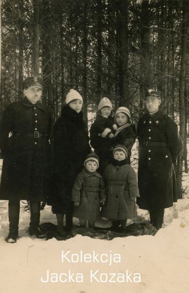 Na zdjęciu znajduje się dwóch żołnierzy Korpusu Ochrony Pogranicza w towarzystwie kobiet i dzieci. Pozują do zdjęcia w porze zimowej. W tle widoczny las.