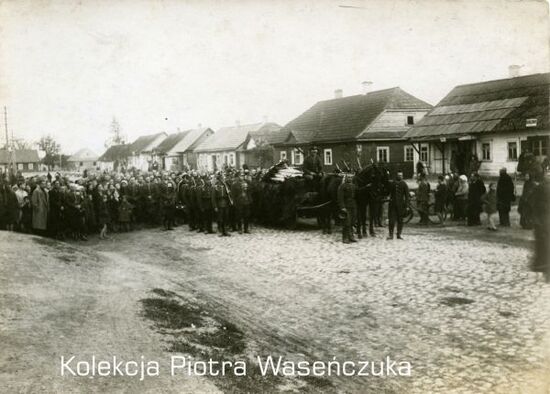Przemarsz żołnierzy KOP przez nieznaną miejscowość- żołnierze w otoczeniu ludności, na pierwszym planie zaprzęg konny, wzdłuż ulicy budynki