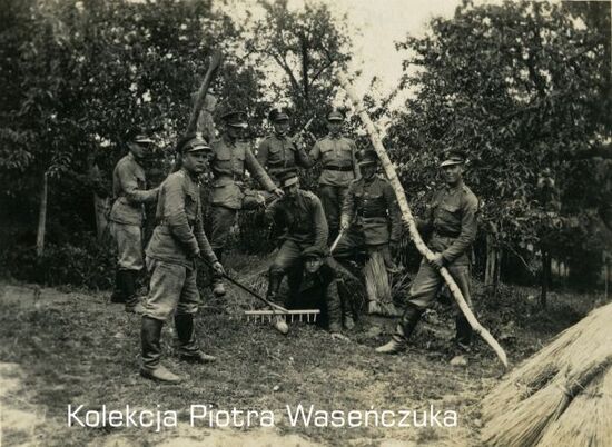 Żołnierskie zabawy- grupa żołnierzy pozująca z nożami, jeden z nich siedzi okrakiem na mężczyźnie jak na koniu, na pierwszym planie żołnierz z grabiami