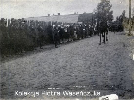 Przemarsz żołnierzy KOP- na pierwszym planie jeździec na koniu, salutujący żołnierze i grupa widzów, na drugim planie- żołnierze w szyku